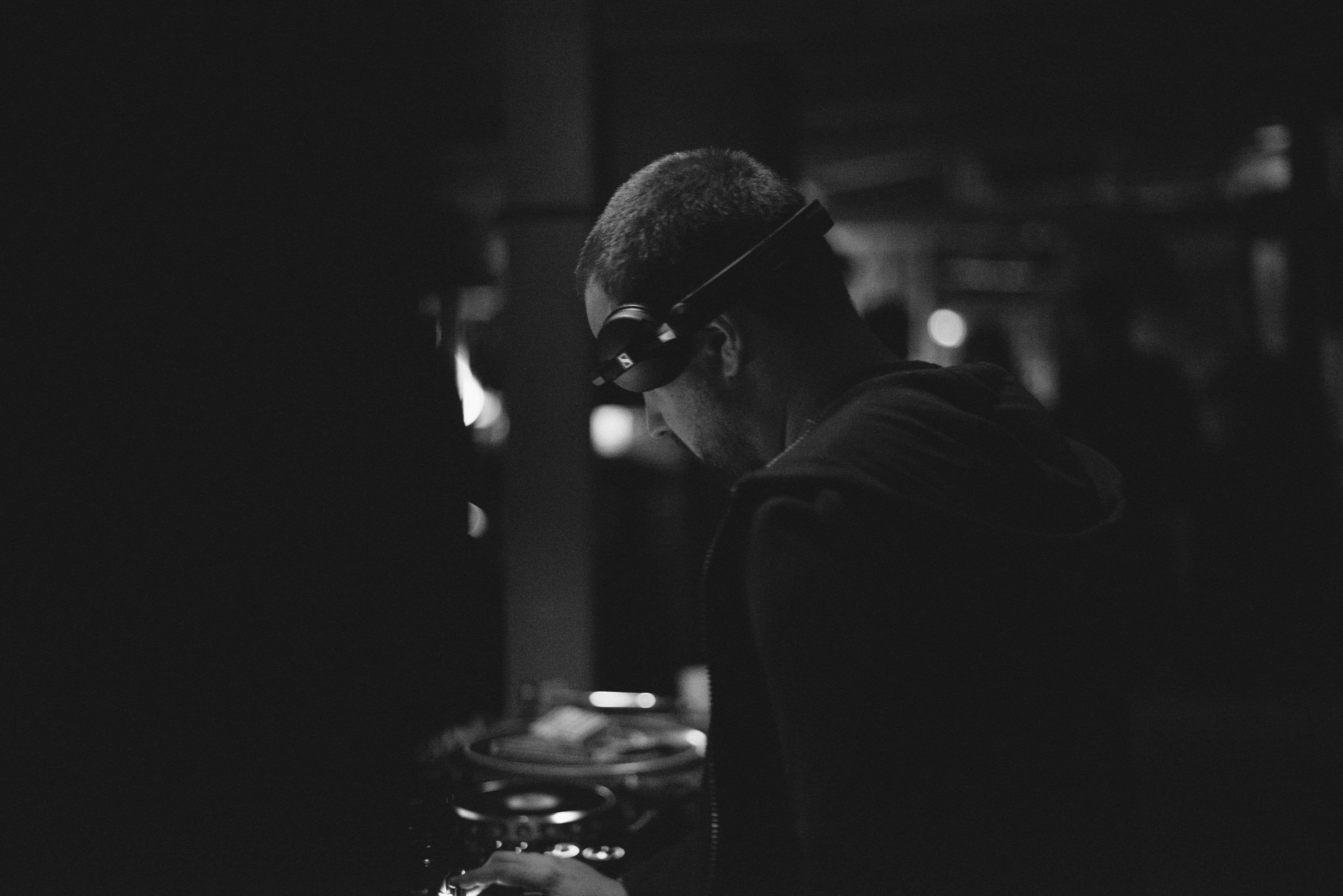A DJ in headphones leaning over the decks, in black and white